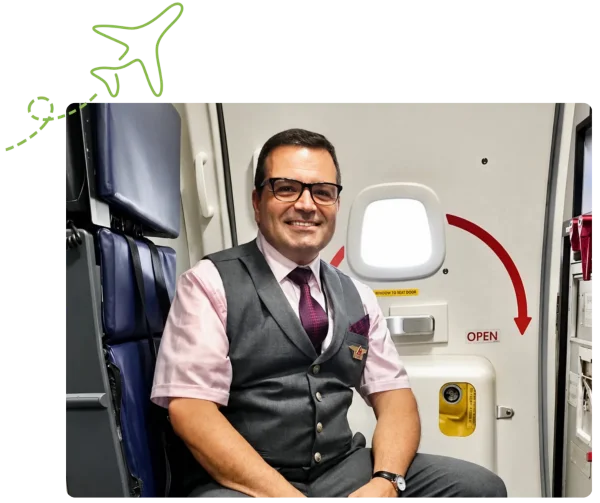 A smiling flight attendant in uniform, sitting in an airplane cabin jump seat.